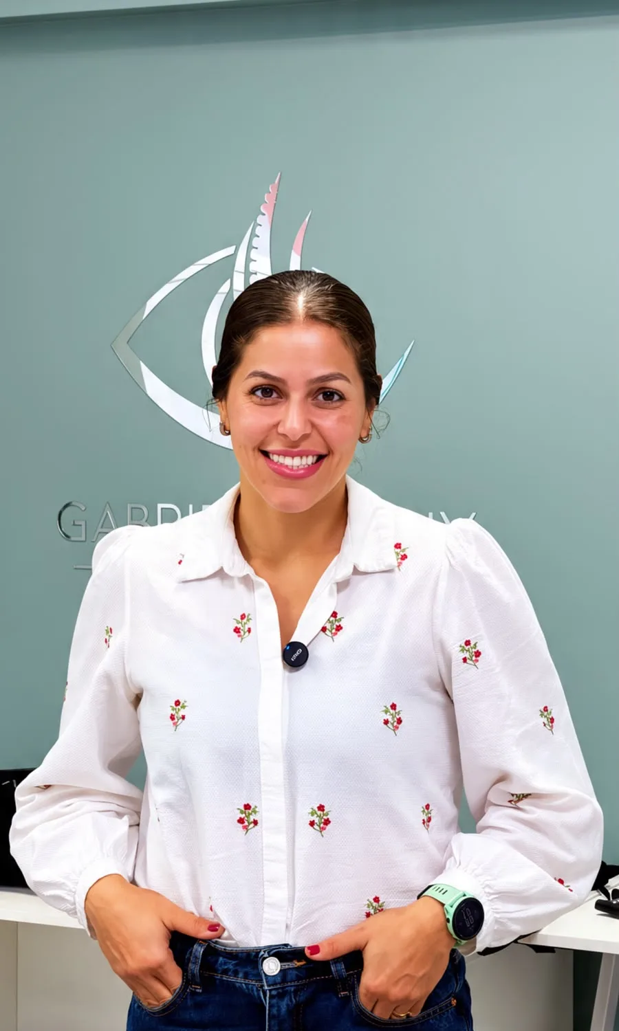 Retrato de Gabriela Kisny sorrindo no consultório, com o logo ao fundo